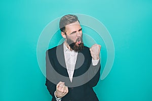 Handsome man is sreaming because of happiness. He is holding his fingers in a fist. Isolated on blue background.