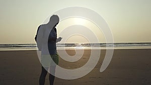 Handsome man standing and dialing message on smartphone on shore. Side view of pleasant man spending time enjoying