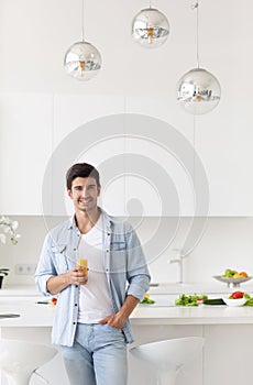 Handsome man standing on the kitchen and drinking orange juice