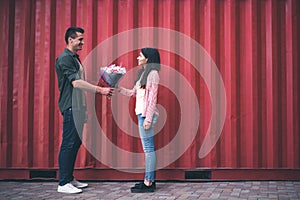 Handsome man standing opposite young woman and giving her flowers