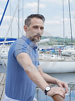 Handsome man standing on pier at barrier with boats background. Bearded attractive man looking on yachts. Man travel