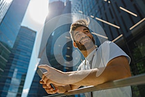 Handsome man standing on skyscrapers background and listen music in headphones and looks away