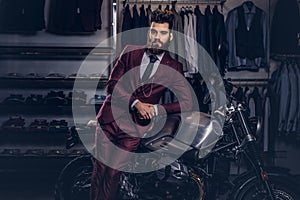 Handsome man with a stylish beard and hair dressed in vintage red suit posing near retro sports motorbike at men`s