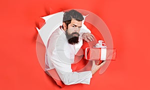 Handsome man in suit with present box looking through paper hole. Bearded man with gift box. Businessman with birthday