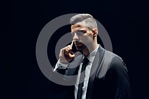 Handsome man in suit talking on mobile phone isolated on dark background