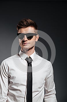 Handsome man in sunglasses and formalwear posing and looking away