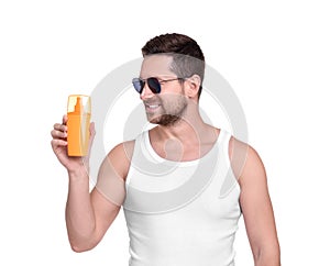 Handsome man in sunglasses holding bottle of sun protection cream on white background
