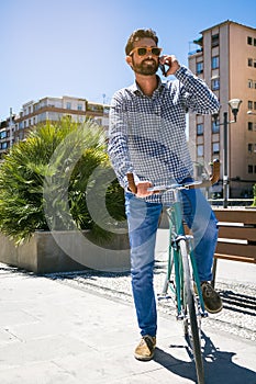 Handsome man with sunglasses smiling and talking on the mobile phone. Fixed Gear bicycle