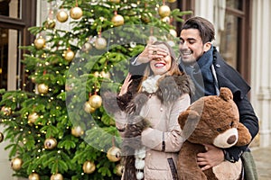 Handsome man surprising his girlfirend witha christmas teddy bea