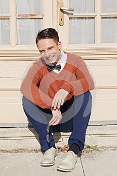 Handsome man in sweater sitting on steps in front of house and p