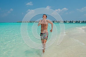 Handsome man in swimming shorts running at the beach at the tropical island