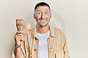 Handsome man with tattoos holding south african 20 rand banknotes looking positive and happy standing and smiling with a confident