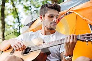 Handsome man tourist singing and playing guitar at touristic tent