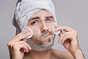 Handsome man with towel on head cleaning face