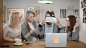 Handsome man tries app for VR helmet virtual reality glasses his friends and colleagues supporting him in modern office