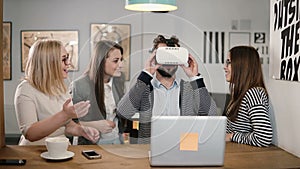 Handsome man tries app for VR helmet virtual reality glasses his friends and colleagues supporting him in modern office