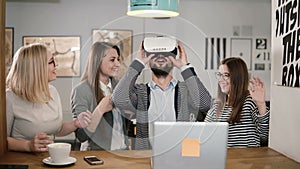Handsome man tries app for VR helmet virtual reality glasses his friends and colleagues supporting him in modern office