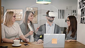 Handsome man tries app for VR helmet virtual reality glasses his friends and colleagues supporting him in modern office