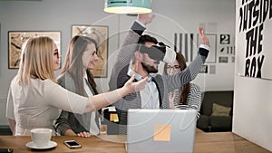 Handsome man tries app for VR helmet virtual reality glasses his friends and colleagues supporting him in modern office