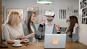 Handsome man tries app for VR helmet virtual reality glasses his friends and colleagues supporting him in modern office