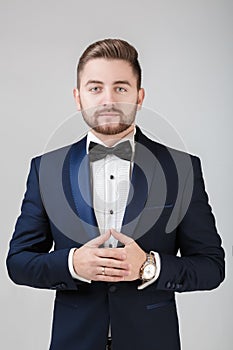 Handsome man in tuxedo and bow tie looking at camera. Fashionable, festive clothing. emcee on grey background