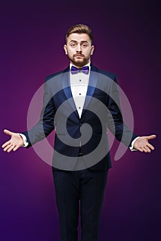 Handsome man in tuxedo and bow tie is surprised, throws his hands. compere in fashionable, festive clothing