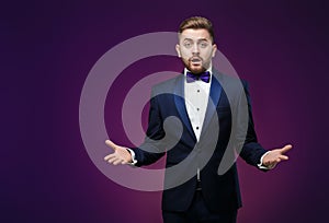 Handsome man in tuxedo and bow tie is surprised, throws his hands. compere in fashionable, festive clothing