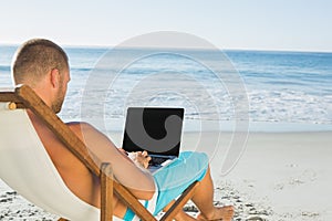 Handsome man typing on his laptop while sitting on his deck chair