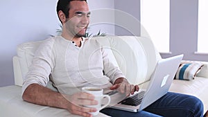 Handsome man using his laptop drinking coffee