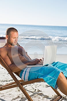 Handsome man using his laptop sitting on his deck chair