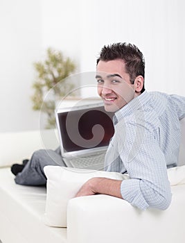 Handsome man is using a laptop, looking at camera and smiling