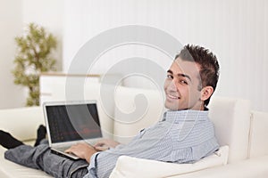 Handsome man is using a laptop, looking at camera and smiling