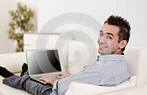 Handsome man is using a laptop, looking at camera and smiling