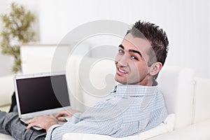 Handsome man is using a laptop, looking at camera and smiling