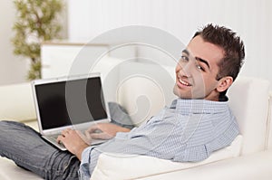 Handsome man is using a laptop, looking at camera and smiling