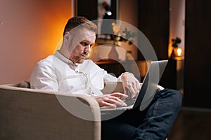 Handsome man using laptop while sitting in soft armchair