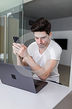 Handsome man using mobile phone and laptop at home