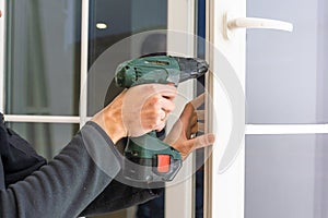 Handsome man using a screwdriver to install a window handle and looking at the camera. Making a house cozy and warm