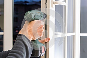 Handsome man using a screwdriver to install a window handle and looking at the camera. Making a house cozy and warm