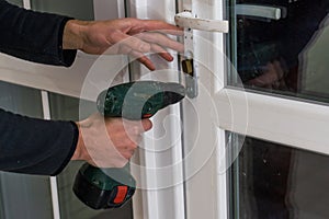 Handsome man using a screwdriver to install a window handle and looking at the camera. Making a house cozy and warm