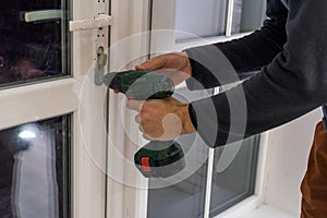 Handsome man using a screwdriver to install a window handle and looking at the camera. Making a house cozy and warm