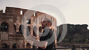 A handsome man visiting Rome, Italy, takes photos near the Colosseum. Guy enjoys the trip, architectural. Slow motion.