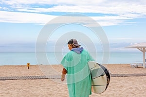 Handsome man walk with white blank surfing board wait for wave to surf spot at sea ocean shore. Back View. Concept of