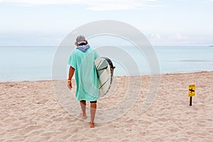 Handsome man walk with white blank surfing board wait for wave to surf spot at sea ocean shore. Back View. Concept of