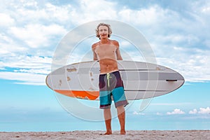Handsome man walk with white blank surfing board wait for wave to surf spot at sea ocean shore. Concept of sport