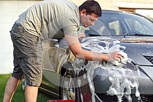 Handsome man washing car with a sponge and foam