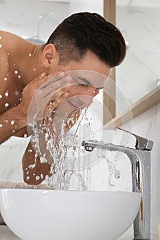 Handsome man washing face over sink in bathroom