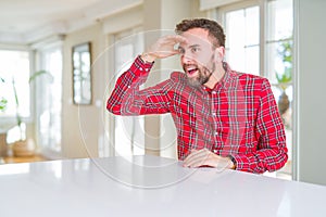 Handsome man wearing colorful shirt very happy and smiling looking far away with hand over head