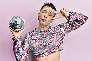 Handsome man wearing make up holding shiny disco ball looking at the camera blowing a kiss being lovely and sexy