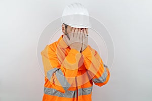 Handsome man wearing reflecting jacket and hardhat with sad expression covering face with hands while crying.